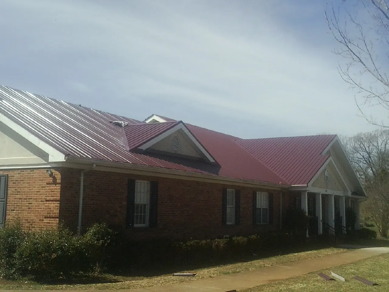 Red metal roof with gabled entries on a long brick building, from a Hail Damage Roof Repair job in La Salle