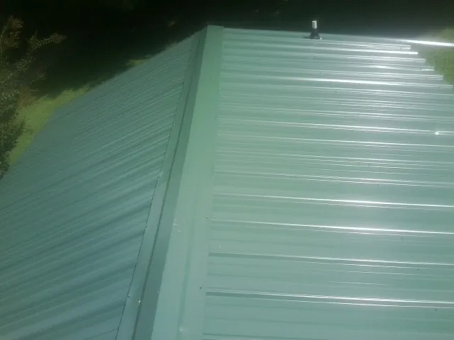 New green metal panels meeting at the ridge of a roof — Flat Roof Repair work by our crew in La Salle